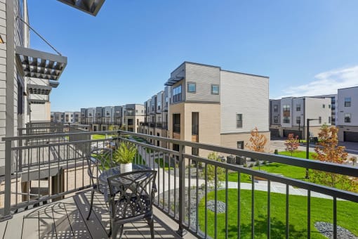 a balcony with a table and chairs overlooking a yard and apartment buildings at Meridian at CityPlace, Woodbury, MN