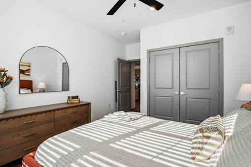 A bedroom with a bed, dresser, mirror, and ceiling fan at The Pullman Luxury Apartment Homes, Atlanta