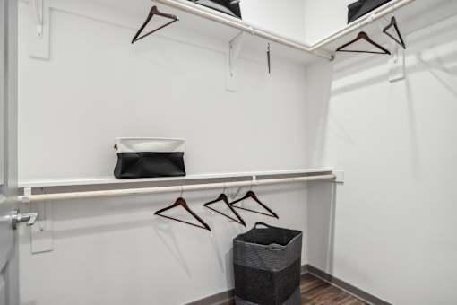 A white closet with clothes hanging and a black bag on a shelf at The Pullman Luxury Apartment Homes, Georgia