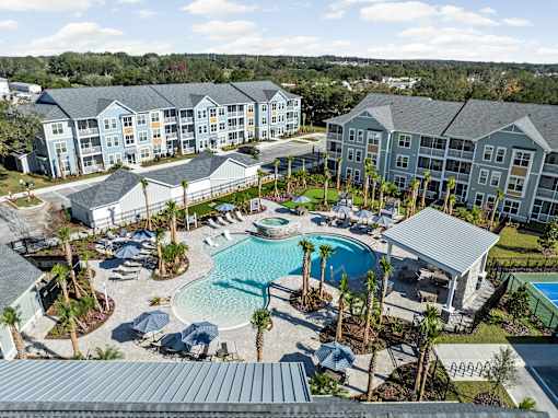 A large swimming pool surrounded by palm trees and lounge chairs in front of apartment buildings.