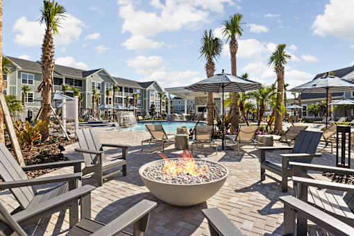 A fire pit sits in the middle of a patio surrounded by chairs and umbrellas.