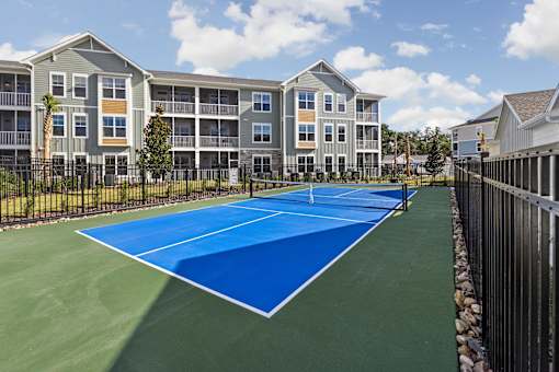 A tennis court is in front of a building with apartments.