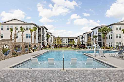 A swimming pool surrounded by lounge chairs and palm trees in front of apartment buildings. at Terrassa Luxury Apartments, Florida, 32084