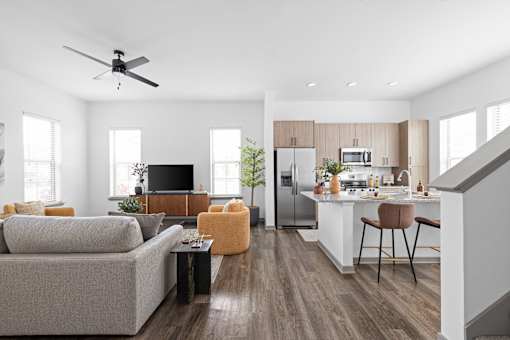 A modern living room with a grey couch, a black television, and a kitchen area in the background.