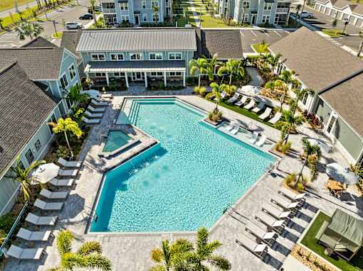 A large swimming pool surrounded by lounge chairs and palm trees. at Junction Apartments in Rockledge, FL