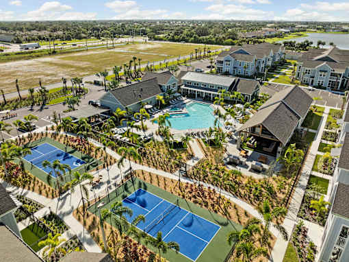 A large building complex with a tennis court in the foreground. at Junction Apartments in Rockledge, FL