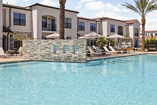 A swimming pool in front of a building with a stone wall and palm trees.at Stella, San Tan Valley Arizona