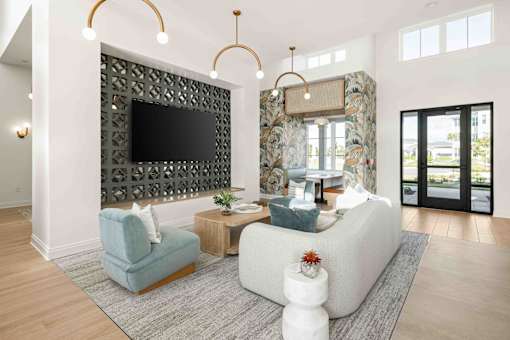 A living room with a grey sofa, a blue armchair, a wooden side table, a television, and a large window at Verity Luxury Apartments, Vero Beach, FL 32960