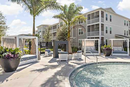 A pool area with a hot tub and lounge chairs in front of a multi-story apartment building at Verity Luxury Apartments, Vero Beach, FL