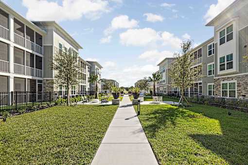 A walkway in the middle of a grassy area with apartment buildings on either side at Verity Luxury Apartments, Vero Beach, FL 32960