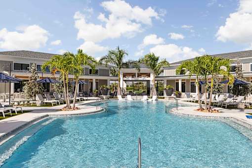 A large swimming pool in front of a building with palm trees at Verity Luxury Apartments, Vero Beach