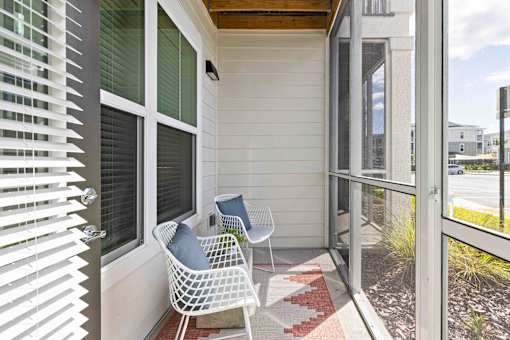 A white chair with a blue pillow is on a porch at Verity Luxury Apartments, Florida 32960