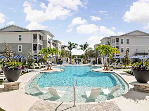 A swimming pool surrounded by white chairs and palm trees at Verity Luxury Apartments, Vero Beach, FL 32960