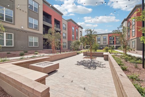 an outdoor area with benches and trees in front of an apartment building at The Maddox Luxury Apartment Homes, Buckeye, AZ 85326  