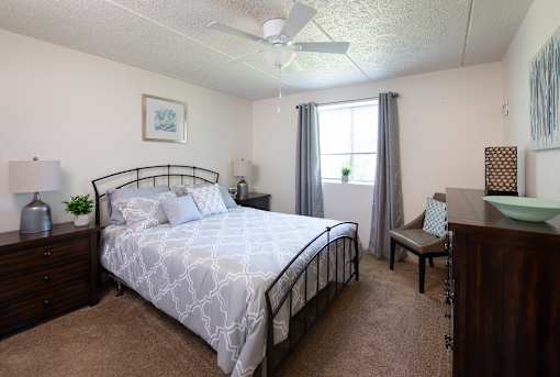 A bedroom with a bed, nightstand, chair, and window.