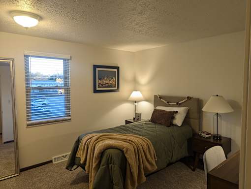A bedroom with a bed, nightstand, and window.
