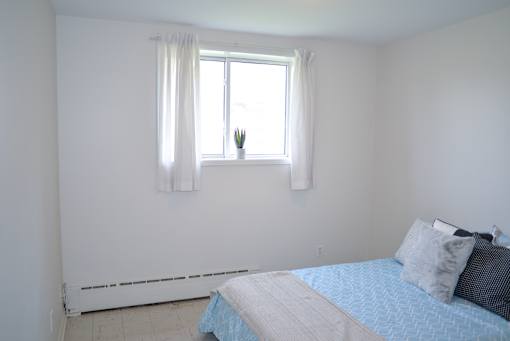 Cozy bedroom with large window and white curtains offering natural light at 359 Edison Apartments.