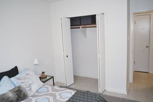A white bedroom with a bed, pillows, a nightstand, and a closet.