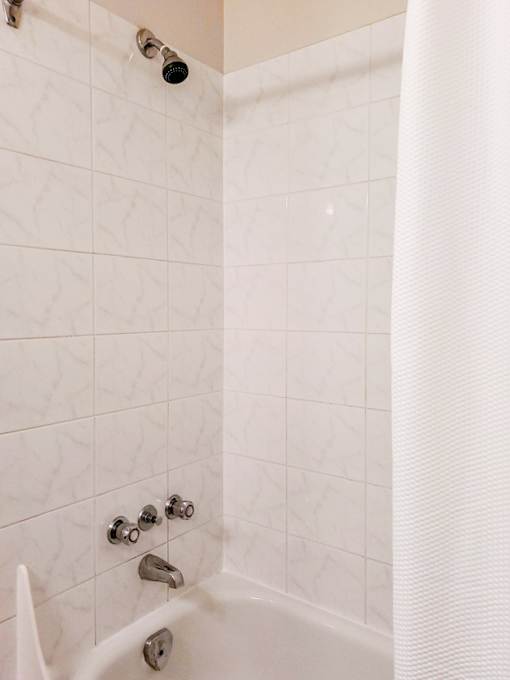 White-tiled bathroom with a bathtub and shower combination at 1025 Munroe Apartments in Winnipeg.