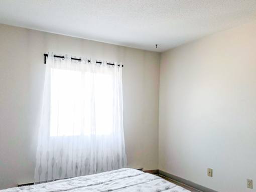 A well-lit bedroom featuring a large window with sheer curtains at 1025 Munroe Apartments in Winnipeg.