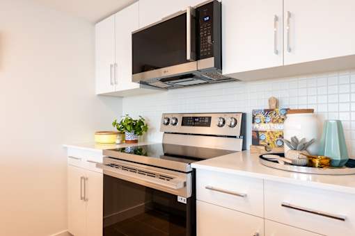 A modern kitchen with white cabinets and a black microwave above the stove.
