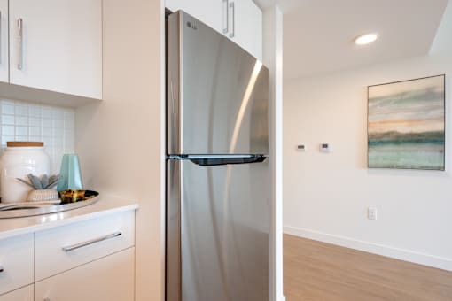 A stainless steel refrigerator stands in a kitchen with white cabinets.