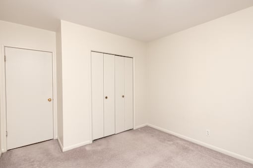 Two white doors in a room with carpeted floor.