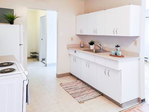 A bright and spacious kitchen with white cabinets, a stainless steel sink, and ample storage at 1025 Munroe pet-friendly apartments in Winnipeg.