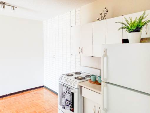 A bright open-concept kitchen and dining area with stylish white cabinets and parquet flooring at 1025 Munroe Apartments.