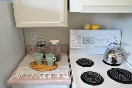 Close-up of kitchen counter with French press, cups, and white stove at 359 Edison Apartments.