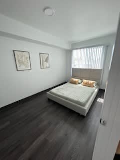 A white bed with a mattress and two pillows is in a room with two pictures on the wall.