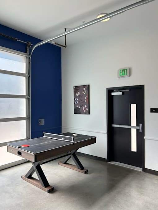 A ping pong table is in the middle of a room with a black door to the right.