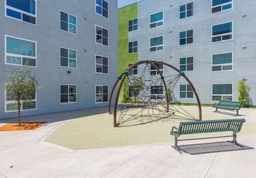 A playground with a swing set and two benches in front of a building.
