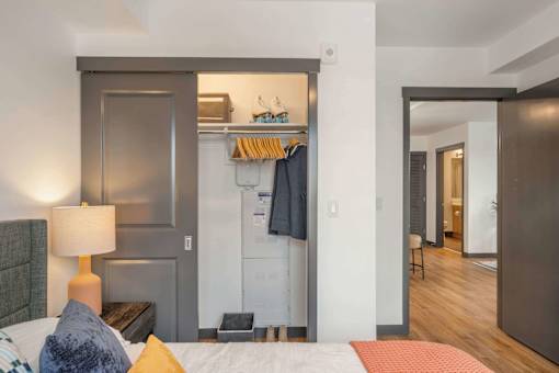 A bedroom with a bed, nightstand, and a closet with clothes hanging at Elevation16 Apartments, Seattle, WA, 98146