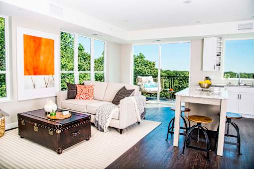 An elegant living room with luxurious stain-resistant plank flooring, a gas fireplace, and expansive windows that offer picturesque views of nature. A seamless transition to a balcony creates a spacious indoor-outdoor connection.