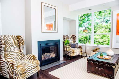An elegant living room with luxurious stain-resistant plank flooring, a gas fireplace, and expansive windows that offer picturesque views of nature. A seamless transition to a balcony creates a spacious indoor-outdoor connection.