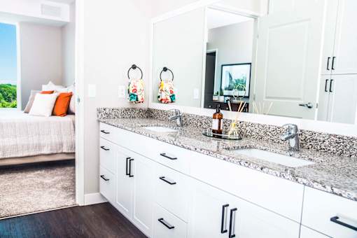 En suite bathroom vanity with granite countertops, stain-resistant plank flooring, and a double sink seamlessly connecting to the luxurious master bedroom.