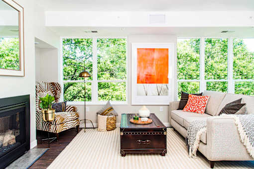An elegant living room with luxurious stain-resistant plank flooring, a gas fireplace, and expansive windows that offer picturesque views of nature. A seamless transition to a balcony creates a spacious indoor-outdoor connection.