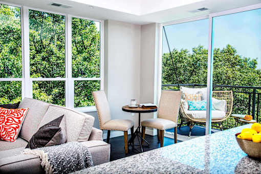 An elegant living room with luxurious stain-resistant plank flooring, a gas fireplace, and expansive windows that offer picturesque views of nature. A seamless transition to a balcony creates a spacious indoor-outdoor connection.