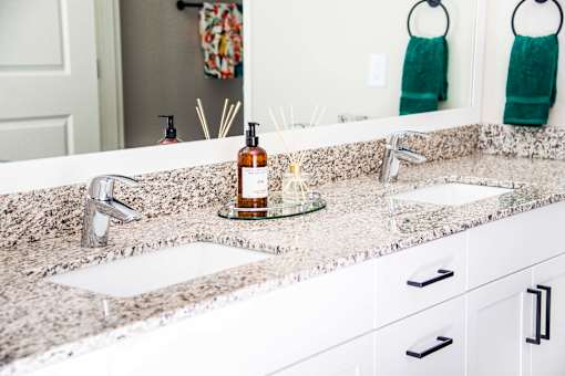 En suite bathroom vanity with granite countertops, stain-resistant plank flooring, and a double sink seamlessly connecting to the luxurious master bedroom.