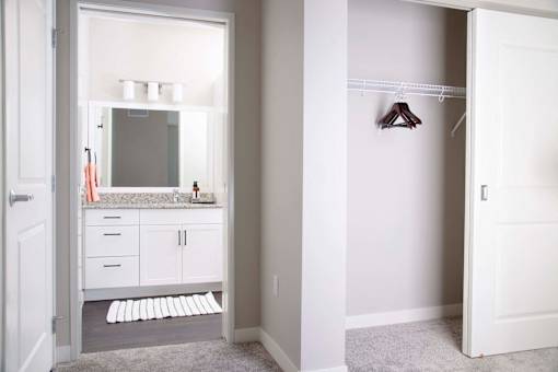 Modern apartment bathroom featuring stain-resistant floors and elegant granite countertops. The adjacent spare bedroom boasts plush carpeting and a spacious closet with sliding doors