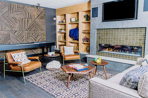 Cozy communal lounge in the apartment complex featuring stylish seating arrangements, a modern flat-screen TV, a warm fireplace, and a tabletop shuffleboard for residents to enjoy.