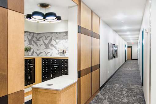 Interior view of a modern apartment complex mail room featuring rows of individual mailboxes neatly arranged along the wall. In the center, there is a flat-screen TV displaying important community announcements and updates.
