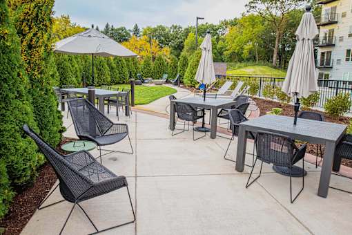 A communal outdoor patio adorned with ample seating arrangements, a cozy gas fireplace, and a fully-equipped grill ready for summer cookouts. The atmosphere radiates warmth and relaxation, offering residents a perfect setting to unwind and socialize amidst the comfort of their living space.