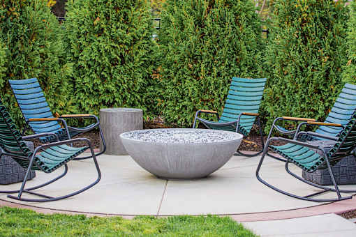 A communal outdoor patio adorned with ample seating arrangements, a cozy gas fireplace, and a fully-equipped grill ready for summer cookouts. The atmosphere radiates warmth and relaxation, offering residents a perfect setting to unwind and socialize amidst the comfort of their living space.