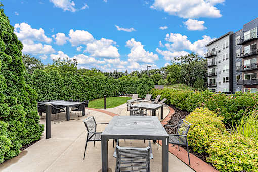 A patio with a table and chairs is surrounded by greenery.