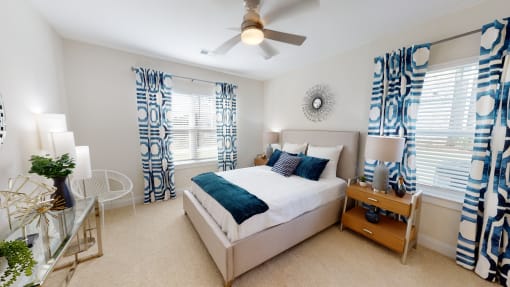 a bedroom with a ceiling fan and two windows with blue curtains at The Retreat at Fuquay-Varina Apartments, Fuquay-Varina