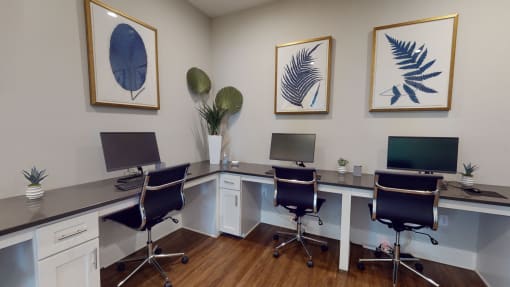 a desk with three computer monitors and three chairs at The Retreat at Fuquay-Varina Apartments, Fuquay-Varina