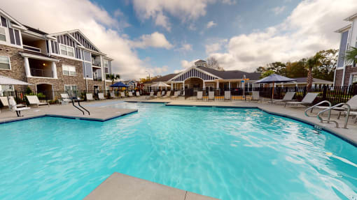 a swimming pool with lounge chairs and umbrellas in front of a building at The Retreat at Fuquay-Varina Apartments, Fuquay-Varina