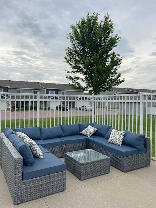 A grey wicker sofa with blue cushions is on a patio.